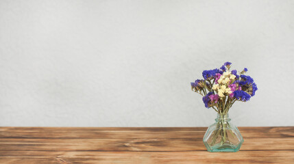 A bouquet of flowers in a small vase. On a wooden table.