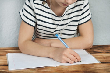 A girl of 8 - 10 years old sitting at the table does her homework. Training
