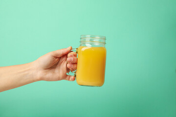 Female hand hold glass jar with orange juice on mint background