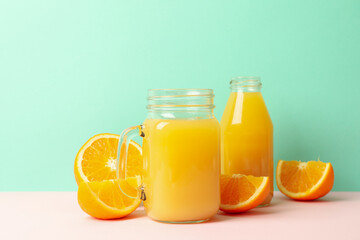 Fototapeta na wymiar Glass jars with orange juice against mint background