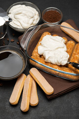 tiramisu dessert cooking - Traditional Italian Savoiardi ladyfingers Biscuits and cream in glass baking dish, coffe maker on dark concrete background
