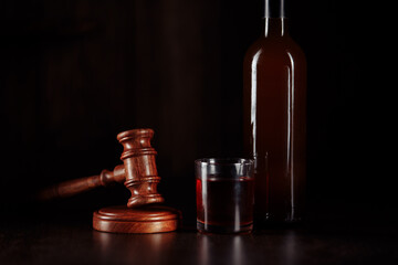 Bottle and glass with whisky and judge gavel, alcohol and crimes concept.