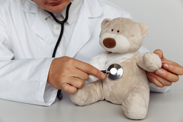 Male doctor with stethoscope and teddy bear in medical office. Children healthcare concept.