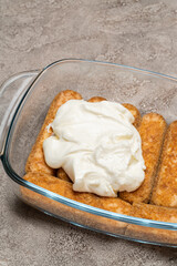 tiramisu dessert cooking - Traditional Italian Savoiardi ladyfingers Biscuits and cream in glass baking dish on concrete background