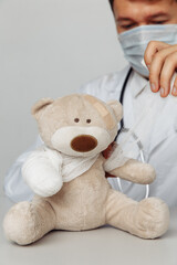 Pediatrician in mask bandage teddy bear in medical office. Close-up. Vertical image. Children healthcare concept.