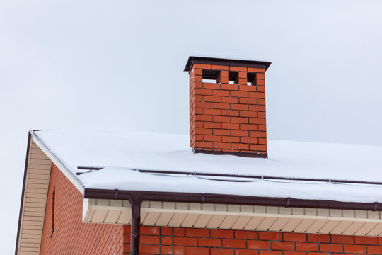 Brick chimney in the snow on the roof of the house.