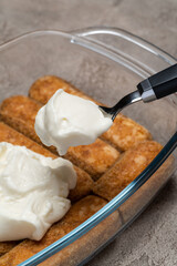 tiramisu dessert cooking - Traditional Italian Savoiardi ladyfingers Biscuits and cream in glass baking dish on concrete background