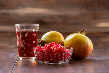 Pomegranate juice in glass, pomegranates and pomegranate seeds in glass bowl on wooden background