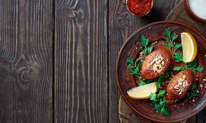 Ichli kyufte (Içli kufta) cutlets or meatballs of meat in shell of bulgur, sprinkled with walnuts, hearty meat dish - cuisine Middle East. Clay plate with cilantro and lemon. Flat lay with copy space