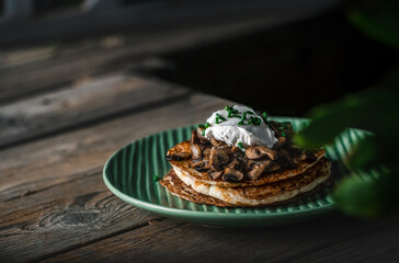 A stack of potato cakes with sour cream on top on a dark rustic wooden background.