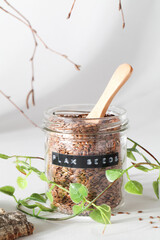flax seeds in glass jar with wooden spoon and natural elements leaves and bark on grey background