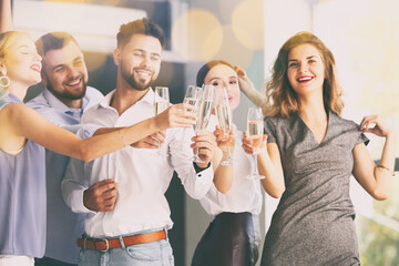 Young people clinking glasses of tasty champagne at party in office