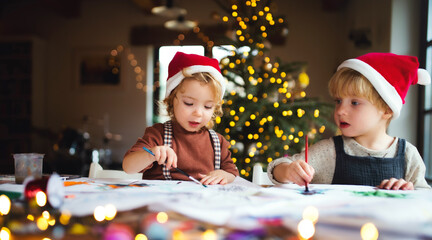 Portrait of small girl and boy indoors at home at Christmas, painting pictures.