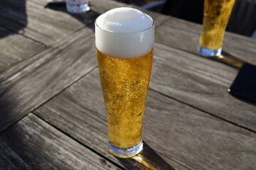 Ein kristallklares Bier mit schönem Bierschaum sonnt sich auf einem Holztisch.