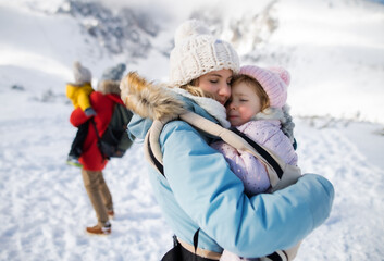 Fototapeta na wymiar Mother with happy small daughter in carrier standing in winter nature, resting.