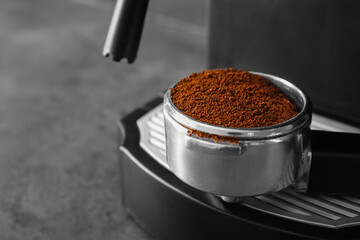 Portafilter with powder near coffee machine on dark background, closeup