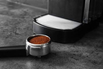 Portafilter with powder near coffee machine on dark background
