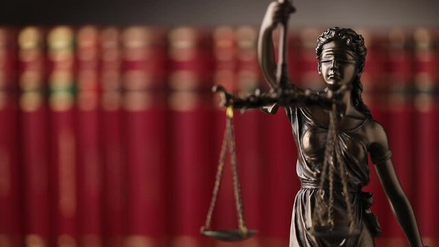 bronze blindfolded goddess representing law statue spinning, holding a scale symbolizing impartiality and two broad sources of law in a university room with a background made of books
