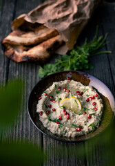 A bowl of freshly made baba ganoush with pomegranate seeds on a dark rustic wooden background.