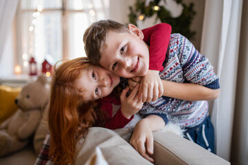 Small girl and boy indoors at home at Christmas, looking at camera.