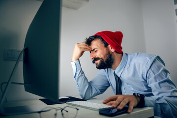 Fototapeta premium Young sad man dressed business casual sitting in his office and holding head. Report is not finished on time.