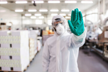 Worker in sterile uniform with rubber gloves holding sprayer with disinfectant and spraying around...