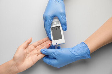 Hands of doctor and diabetic woman with glucometer on light background