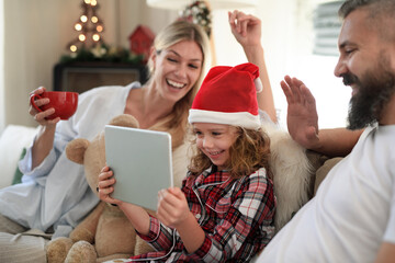 Family with small daughter indoors at home at Christmas, having video call.