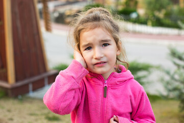 A little girl in a pink hoodie with a sad and tearful face is holding her ear. Ear pain, otitis...