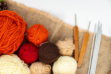 Fototapeta na wymiar Cozy hobby concept for autumn. Balls of yarn (brown, red, orange, beige) for knitting, crochet hooks, knitting needles on sackcloth.
