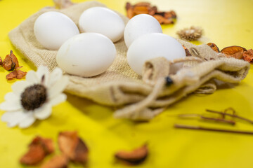 Low angle shot of five eggs on a jute bag with decorated flowers on yellow background