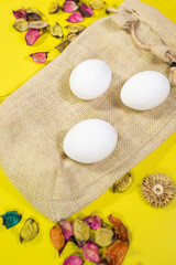  Three eggs on jute bag with decorated flowers and leaf's on yellow background