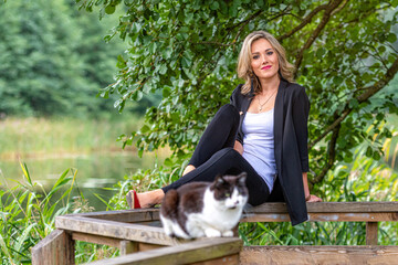 Obraz premium blonde woman and cat siting on a railing wooden walkway above the pound