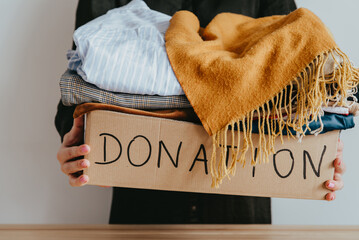 Woman holding cardboard donation box full with clothes. Concept of volunteering work, donation and...