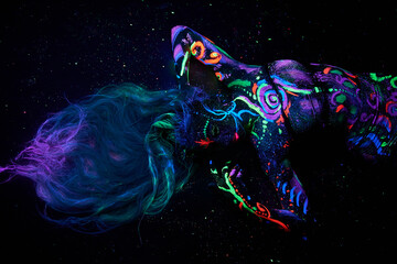 Art woman body art on the body dancing in ultraviolet light. Bright abstract drawings on the woman body neon color. Colored hair and face