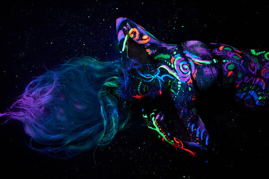 Art woman body art on the body dancing in ultraviolet light. Bright abstract drawings on the woman body neon color. Colored hair and face
