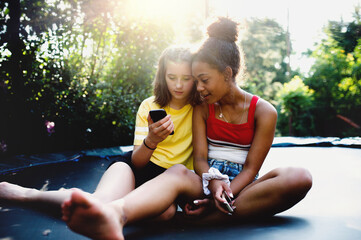 Front view of young teenager girls friends outdoors in garden, using smartphone.