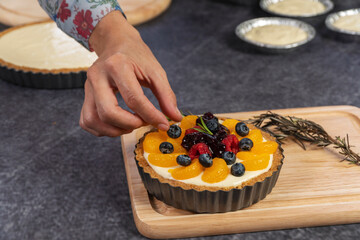 Hand of young woman decorating blackberry pie using fresh fruits on table. Homemade bakery concept.