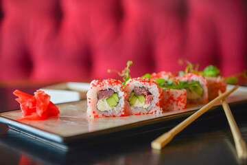 Salmon and caviar sushi rolls served on a traditional plate on a wooden table in a restaurant.