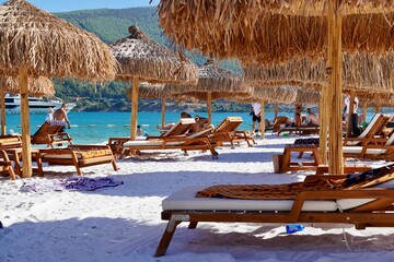 Bodrum, Turkey - August, 2020: Snow-white beach of Lux Hotel with emerald water of Aegean Sea. Yachts.People sunbathing on the beach. Sunbeds on the beach. Relaxing Deluxe Leisure Conception