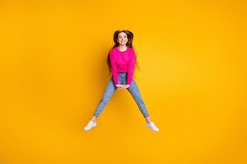 Full length photo of charming young woman jump hold hands wear pink pullover jeans sneakers isolated yellow color background