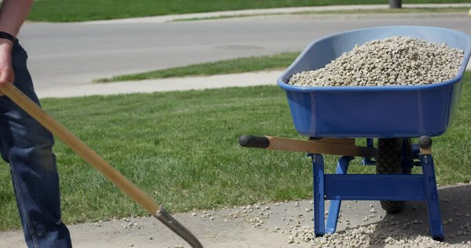 Man fills wheelbarrow with small rocks on drive way - wide shot side profile