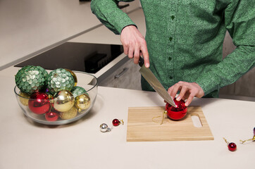 man with knife in his hand cuts salad of decorated Christmas balls. Concept of preparation for the holiday