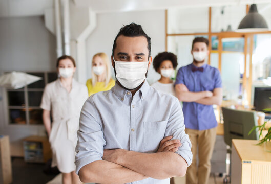 business, health and people concept - young man with beard over creative team wearing face protective medical mask for protection from virus disease at office