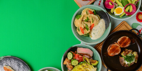 Variety of food dishes on bright green background. Table covere with food flat lay, top view, frame.