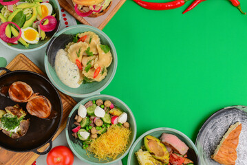 Variety of food dishes on bright green background. Table covere with food flat lay, top view, frame.