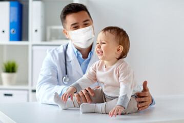 medicine, healtcare, pediatry and people concept - happy doctor or pediatrician wearing face protective mask for protection from virus disease with baby on medical exam at clinic - obrazy, fototapety, plakaty