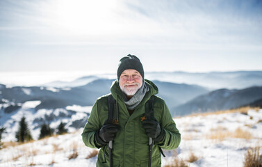 Fototapeta na wymiar Portrait of senior man standing in snow-covered winter nature, looking at camera.