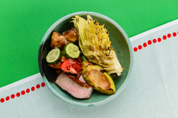 Delicious fried vegetables, fried cabbage with meat and cucumbers in a bowl over bright green background.