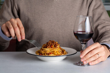 A man eating traditional italian pasta tagliatelle al ragù, also known as pasta bolognese. Red whine glass. Life style photo.